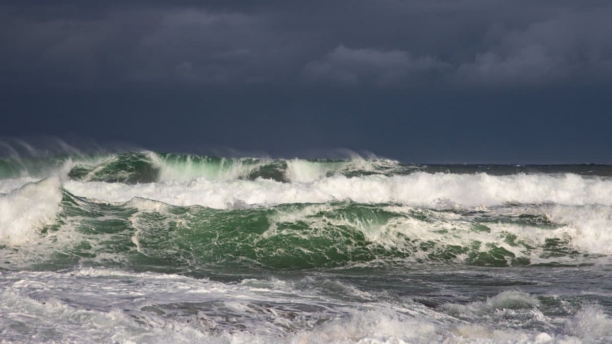 Powerful ocean waves crash under dark stormy clouds, capturing nature's raw force.