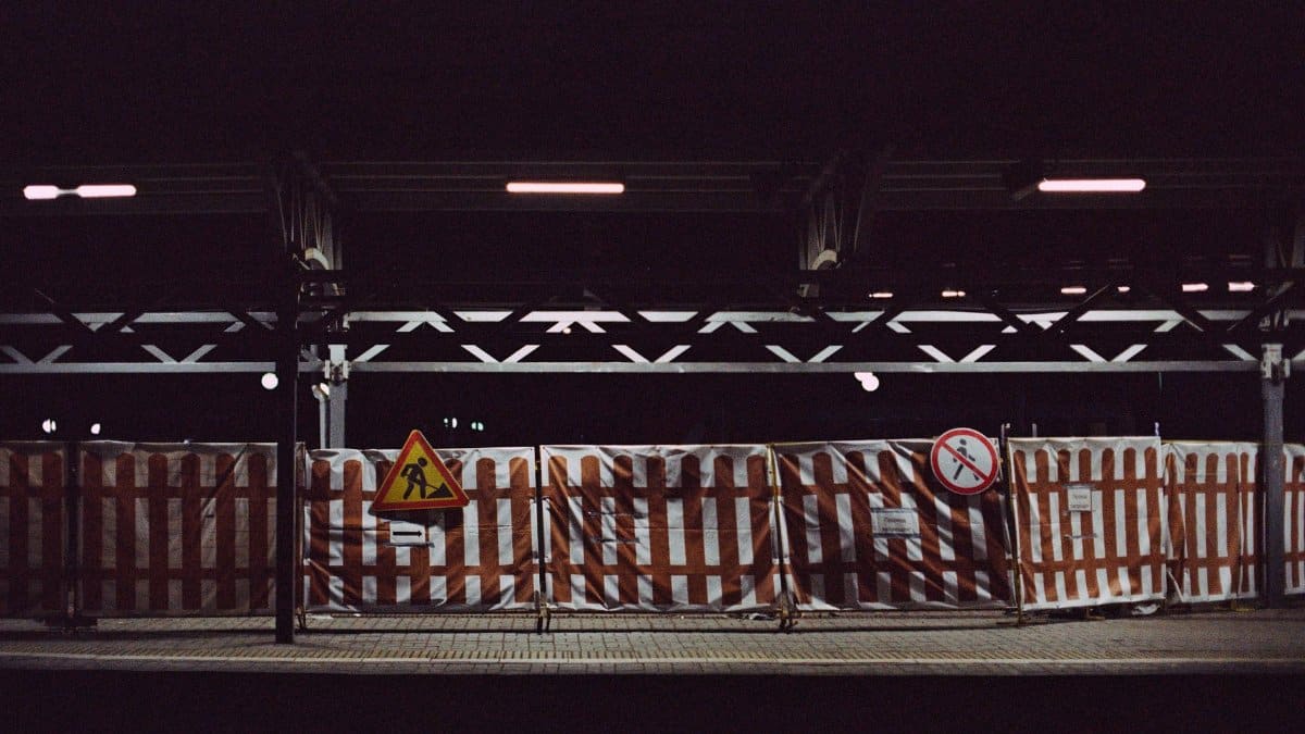 Railway station platform at night with construction signs and fenced barriers, highlighting urban development.