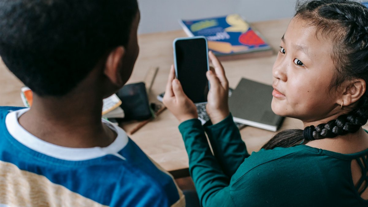 From above of adorable little Asian girl showing mobile phone to unrecognizable African American boy during break in classroom