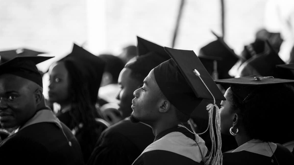 A group of students in graduation gowns and mortarboards attending a ceremony.