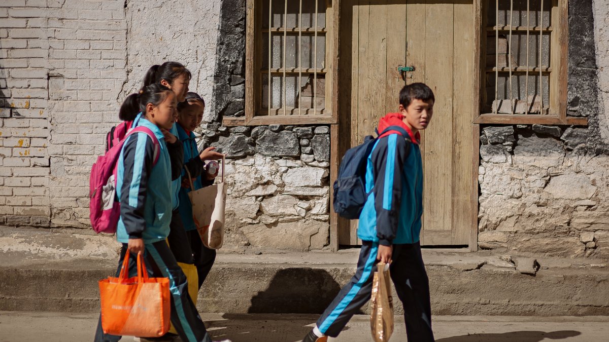 Four students in matching uniforms walk past a rustic stone wall, focusing on a journey.
