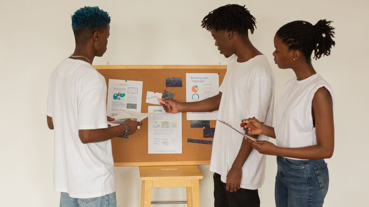 African American students in casual clothes standing near whiteboard and discussing details of project