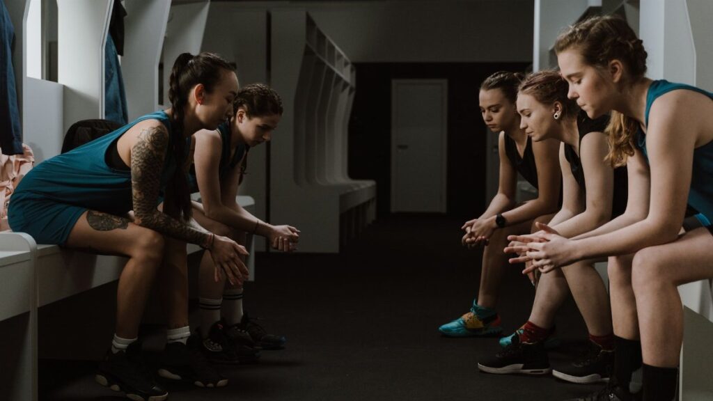 A group of female athletes sitting in a locker room, reflecting before a game.
