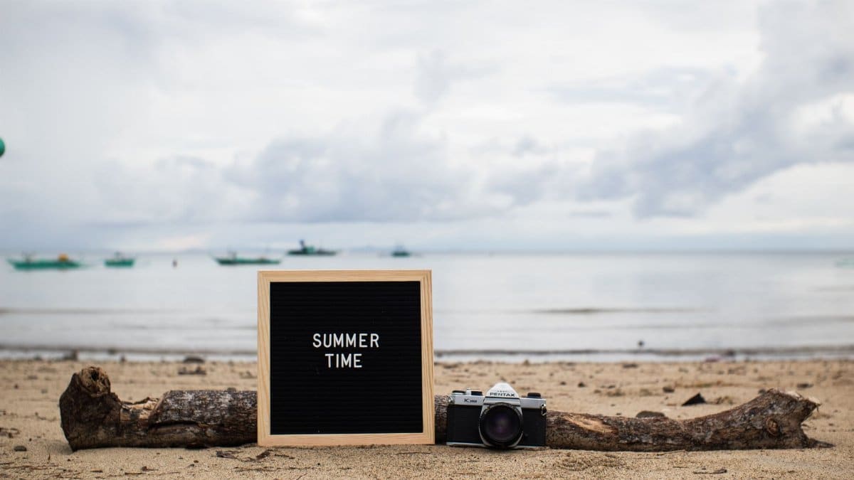 Beach scene with a message board reading 'SUMMER TIME' and a vintage camera.