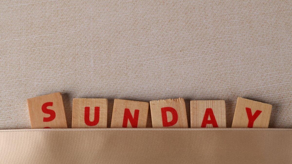 Wooden letter blocks spelling 'Sunday' against fabric surface.
