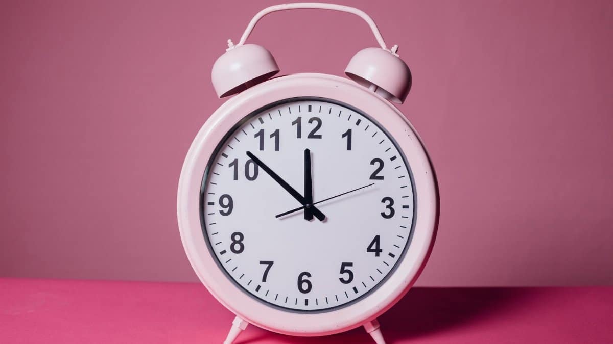 Pink retro alarm clock on a pastel pink background symbolizing time and punctuality.