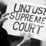 Black and white photo of a protester holding a sign saying 'Unjust Supreme Court' during a demonstration.