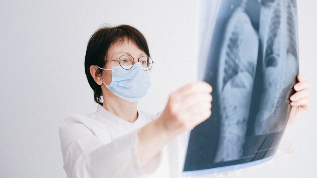 Doctor analyzes lung x-ray wearing a mask in a clinical setting.