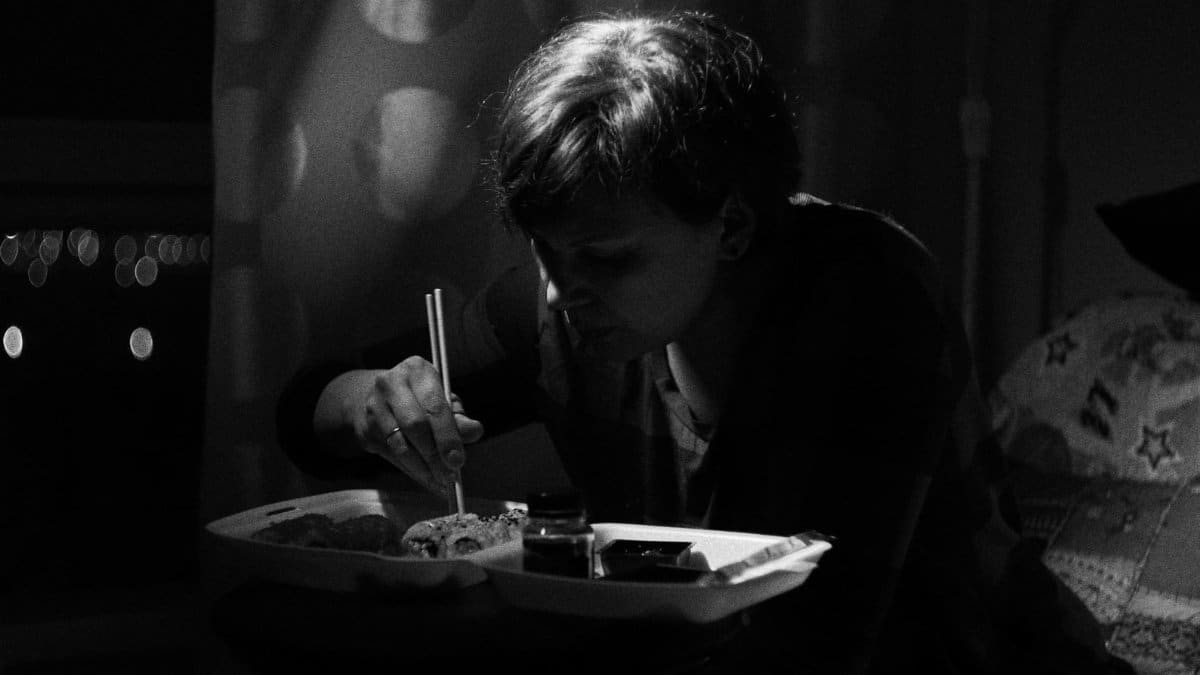Person eating sushi alone at night in a dimly lit room, conveying solitude.