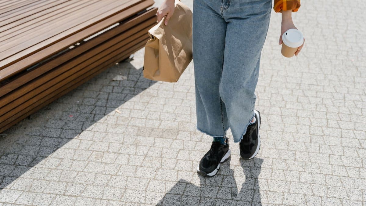 Casual person in denim jeans walking with takeaway items on a sunny day.
