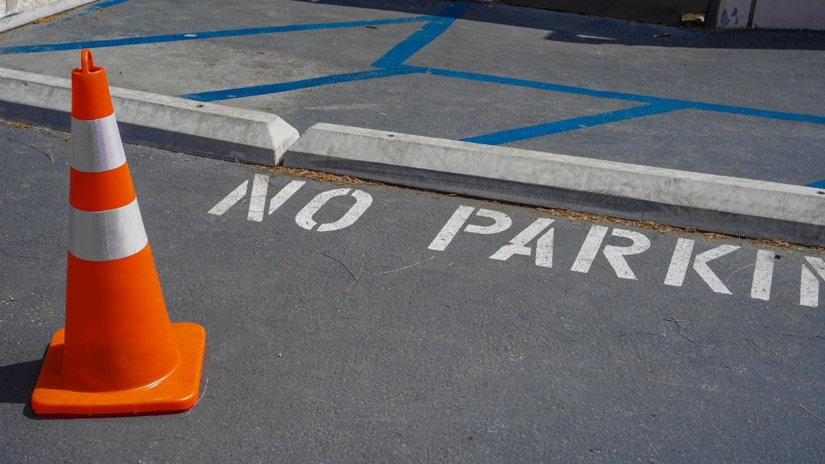 An orange traffic cone on a no parking zone with blue lines in a city street.