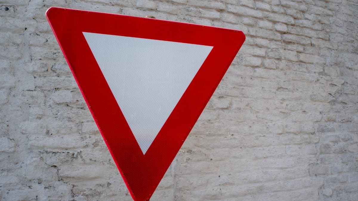 Close-up of red yield traffic sign against a textured white brick wall.