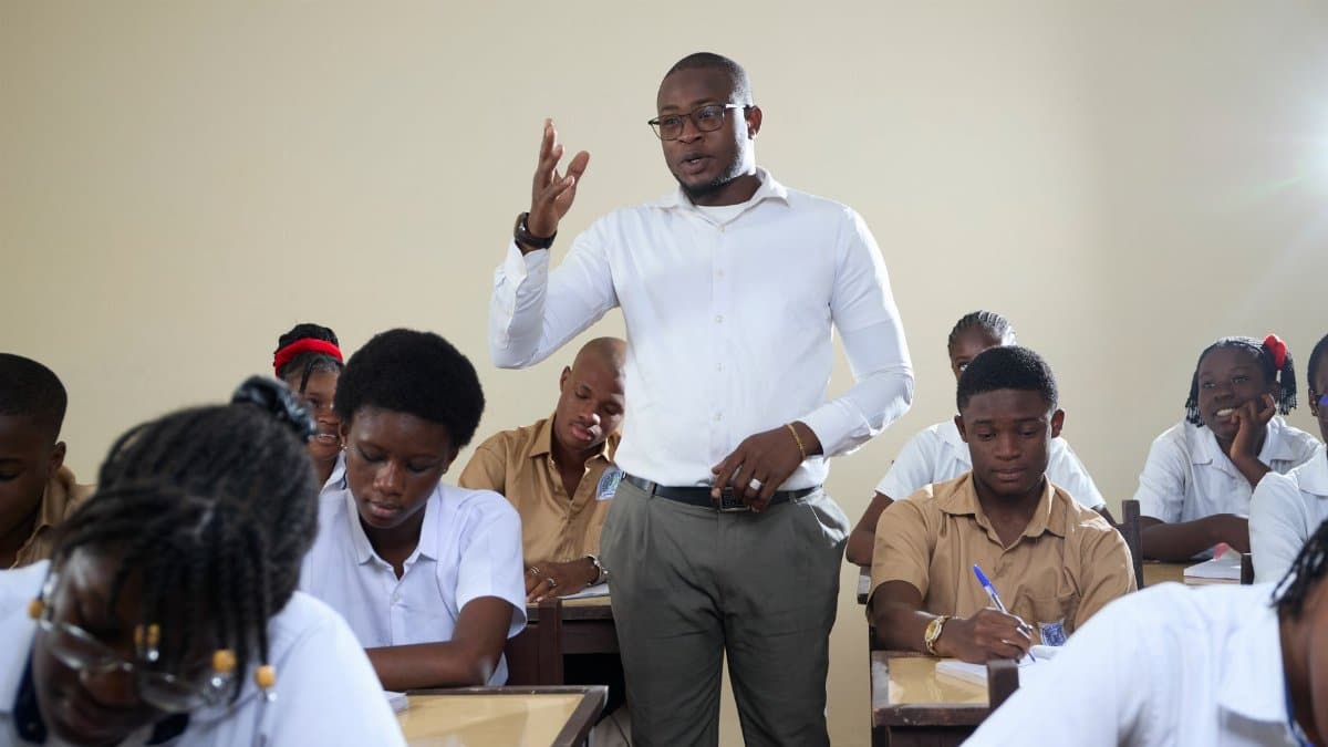 Teacher interacting with high school students in a classroom setting.