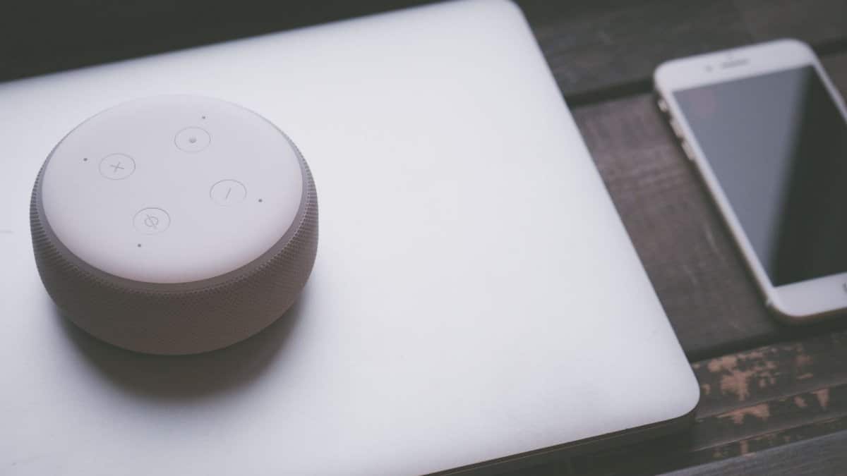 A smart speaker, laptop, and smartphone array representing modern technology lifestyle on a wooden surface.