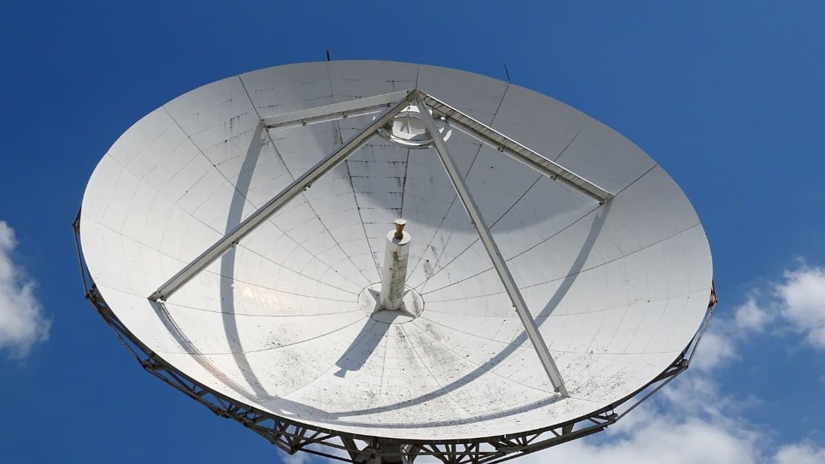 A low angle view of a large satellite dish against a clear blue sky with scattered clouds.