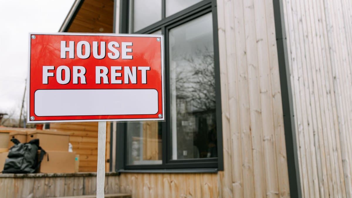 Red 'House for Rent' sign outside modern wooden house.