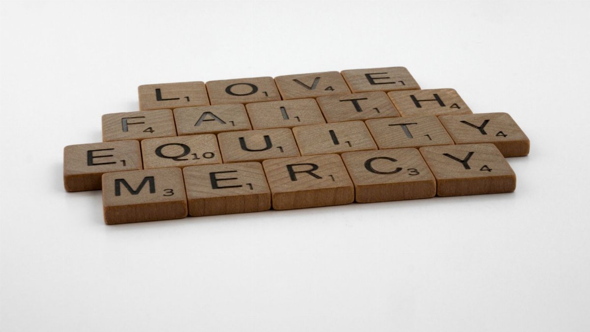 Wooden letter tiles spelling love, faith, equity, and mercy, arranged on a neutral background.