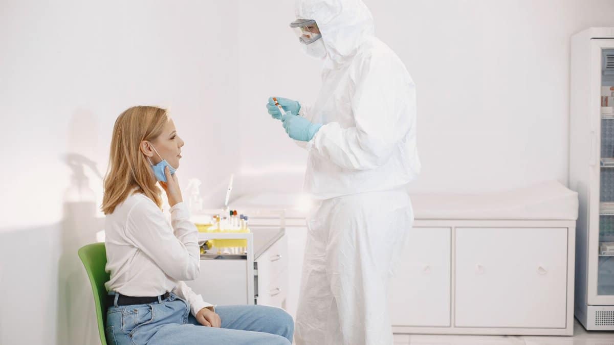 Medical professional in PPE collecting a swab sample from a patient in a clinical setting.