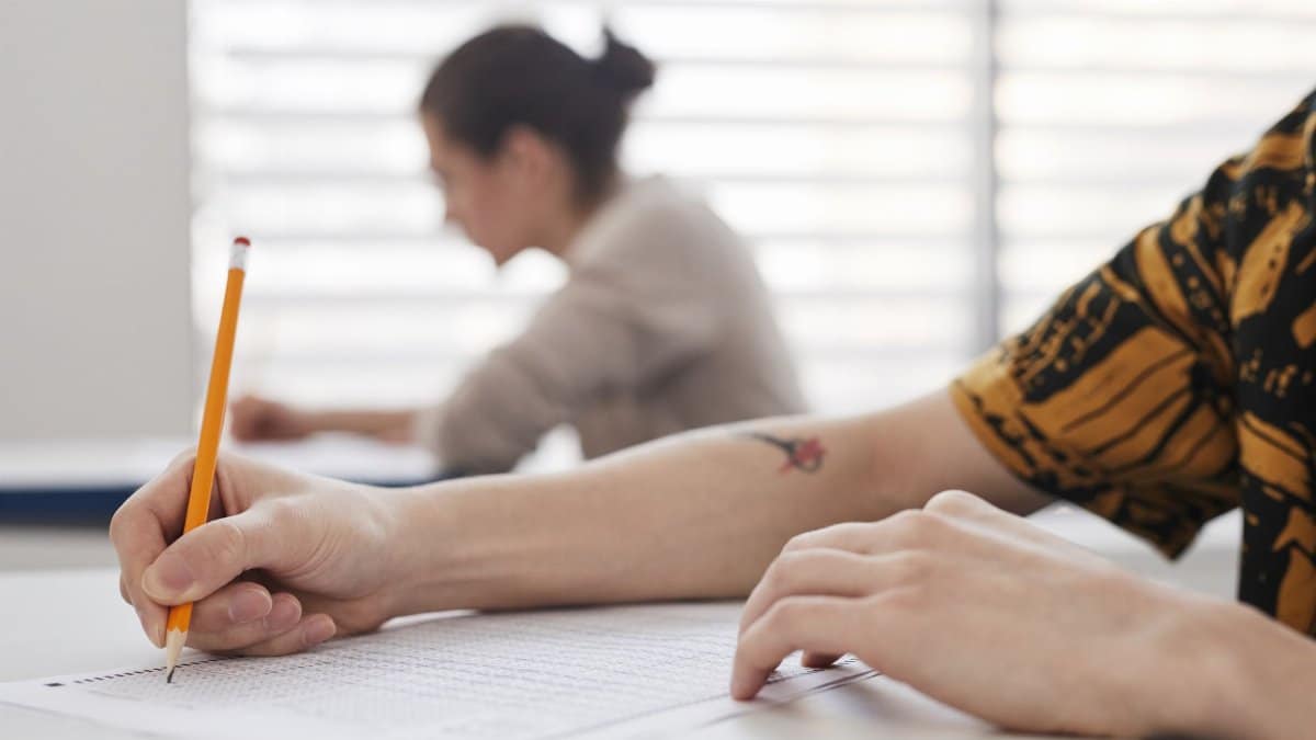 Close-up of student's hands writing on exam sheet, indoors with blurred background.