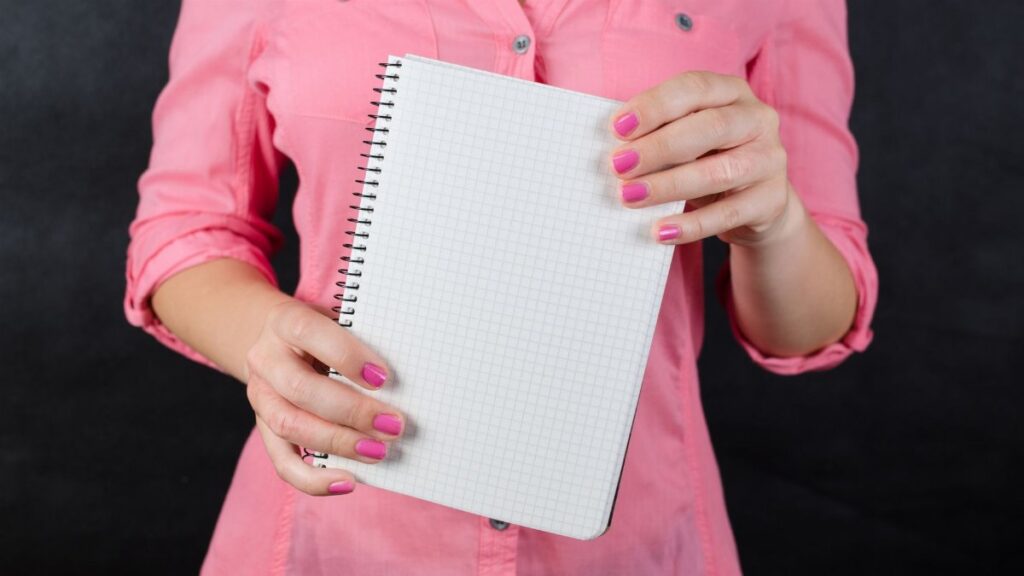 A woman in a pink shirt holds a blank notepad, ideal for mockup use.