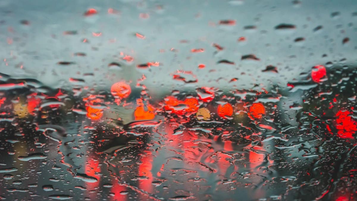 Raindrops on a window creating a blurry view with red bokeh lights shining through in Dallas.