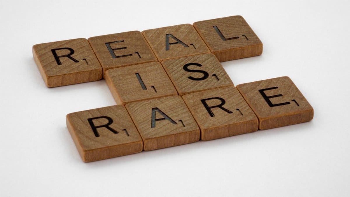 Wooden Scrabble tiles arranged to spell 'Real is Rare' on a white background.