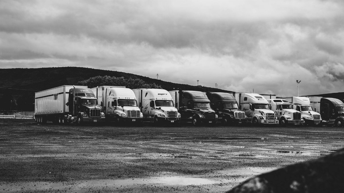 Row of parked semi trucks in a rainy lot, captured in a dramatic black and white setting.