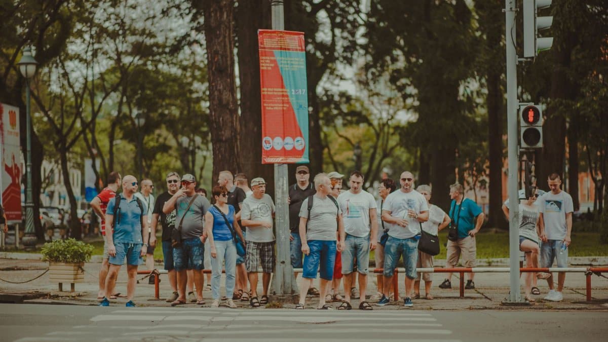 A diverse group of adults stands at a city crosswalk, waiting to cross the street on a clear day.