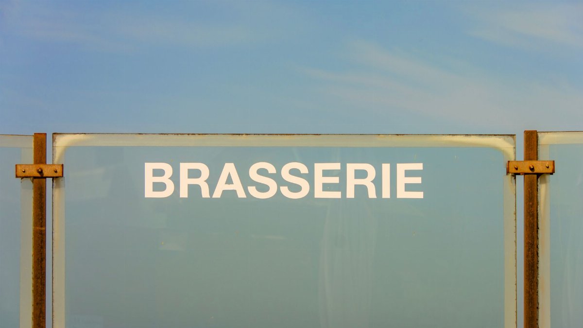 Glass brasserie sign with metallic support under a clear blue sky.