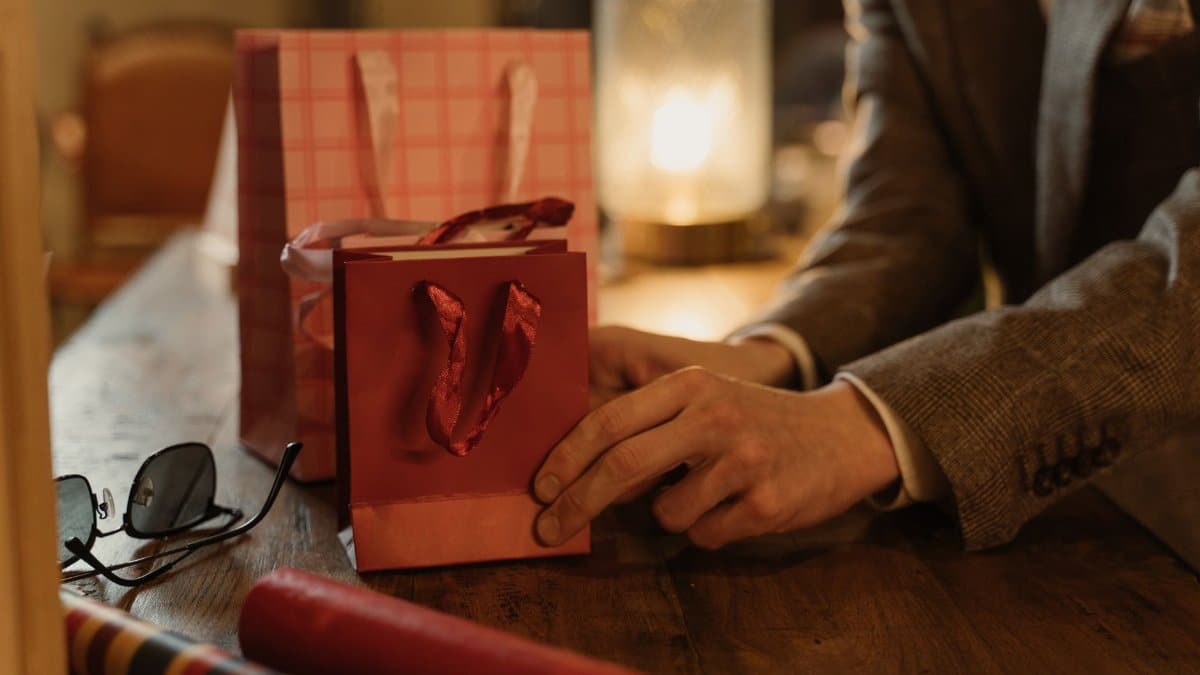 Close-up of hands arranging gift bags on a wooden table, ideal for commerce and business themes.