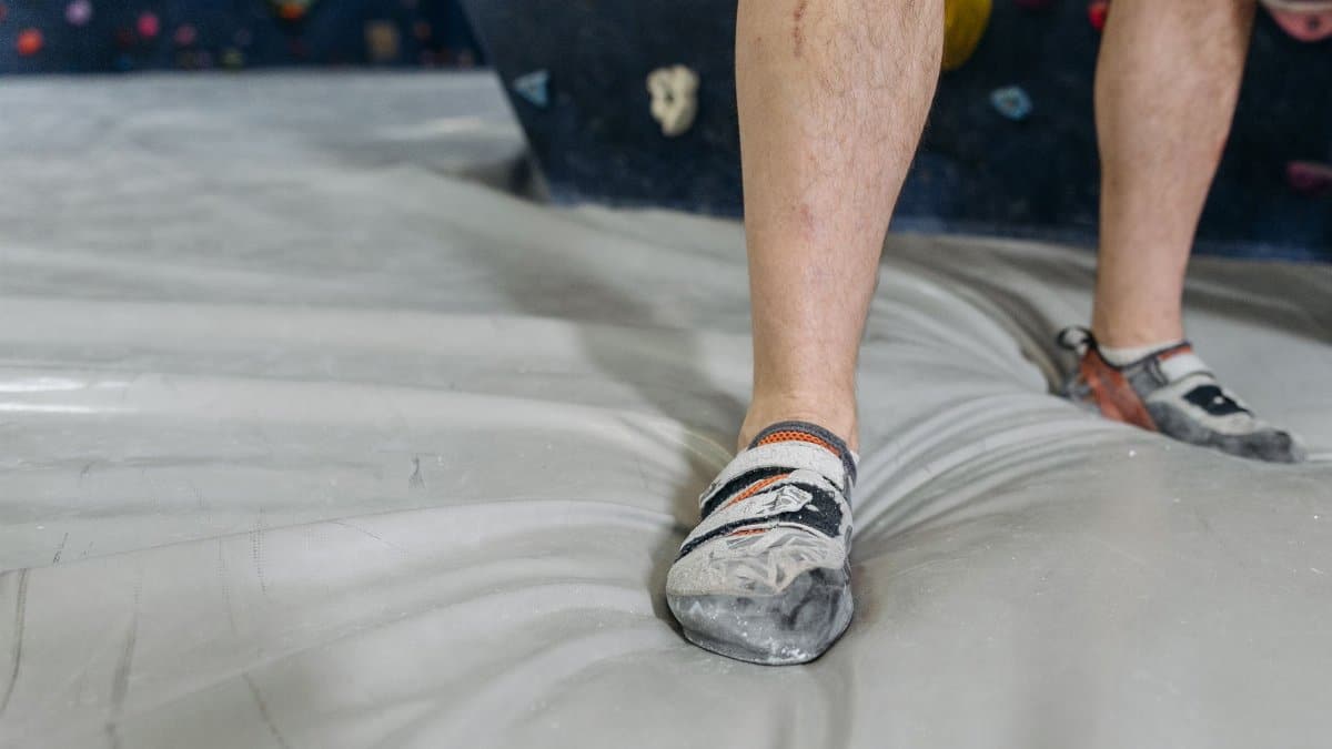 A climber's legs in climbing shoes on a gym floor, close-up view.