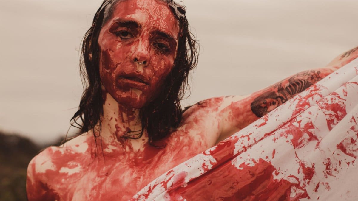 A striking artistic portrait featuring a person covered in red paint outdoors.