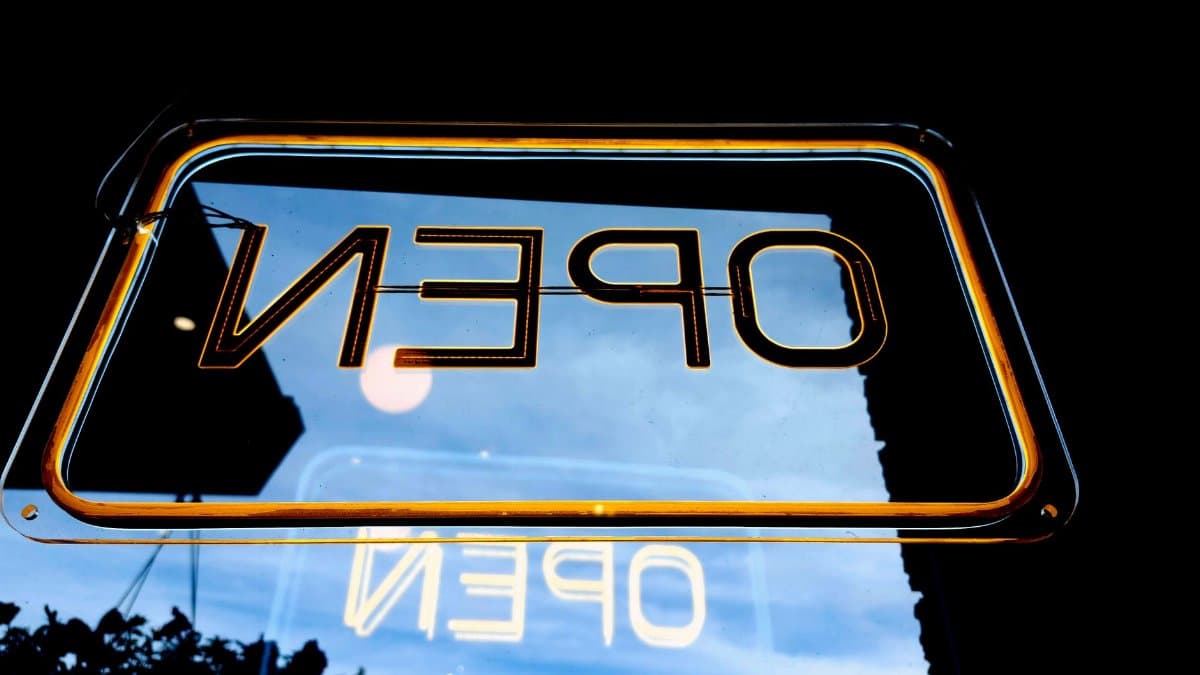 Upside-down neon 'Open' sign glowing warmly, reflecting urban night ambiance.