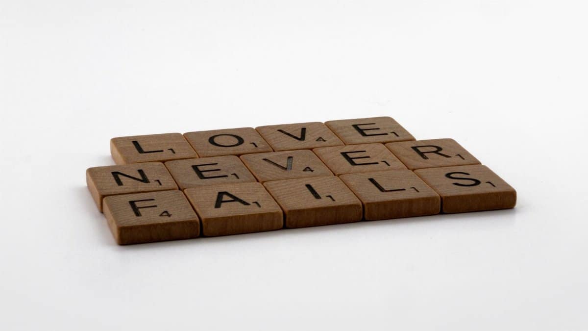 Scrabble tiles arranged to spell 'Love Never Fails' on a clean white background, symbolizing enduring love.