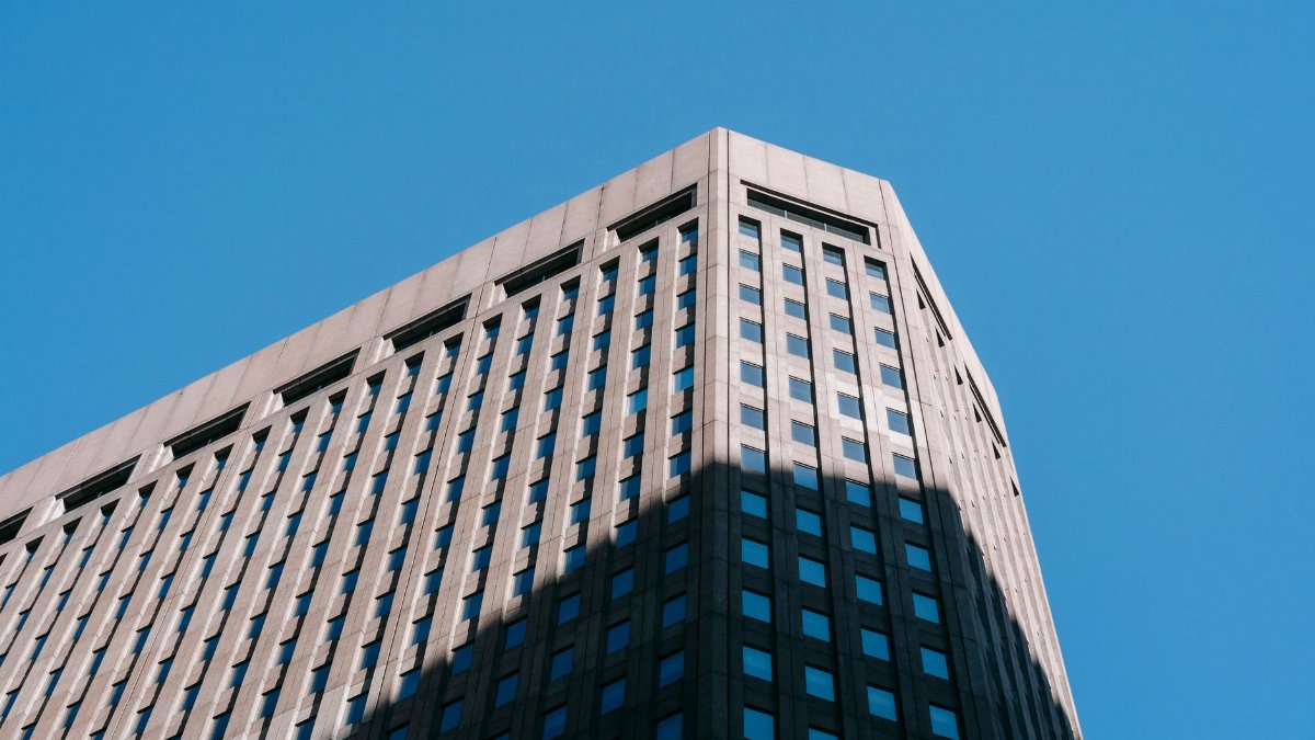From below of tall multistory building of financial company in megalopolis against blue sky