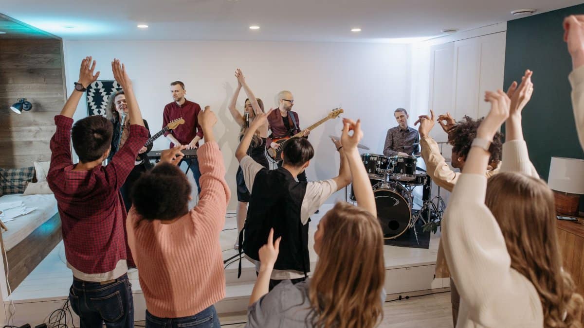 A lively home concert with a band performing and an enthusiastic group dancing indoors.