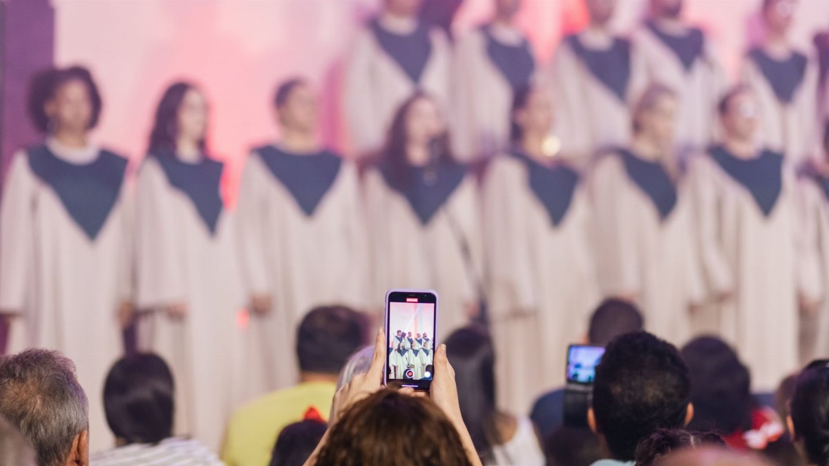 An audience records a live choir performance with smartphones indoors.