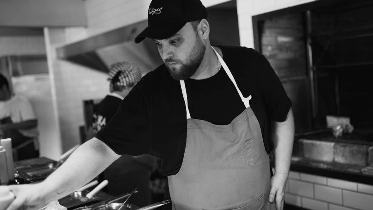 A focused chef working in a professional kitchen, wearing an apron and cap.