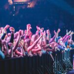 Excited crowd with hands up at a vibrant live music concert indoors.
