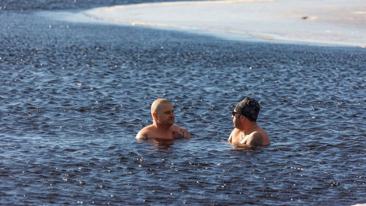 Two men enjoying winter swimming in icy waters, showcasing extreme cold exposure.