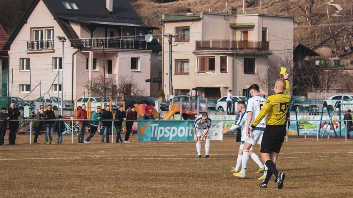 A lively soccer match in Domaniža, Slovakia, showcasing a referee giving a yellow card.