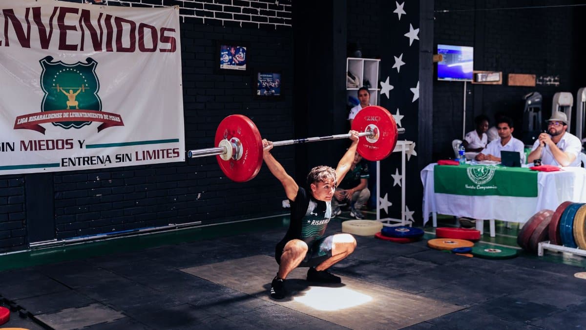 Athlete executing a snatch lift at a weightlifting competition indoors.