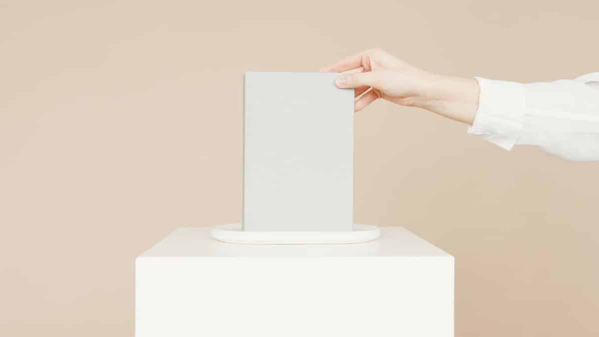 A hand places a blank book on a pedestal against a neutral background, perfect for mockups.