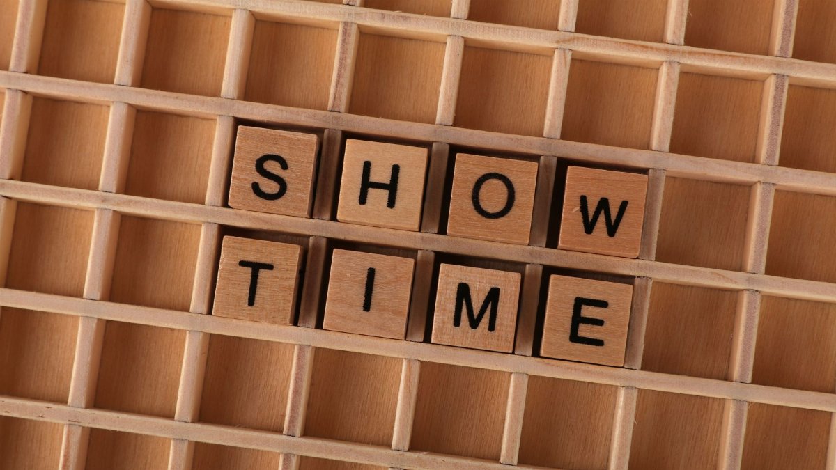Wooden letter tiles arranged to form the words SHOW TIME on a wooden grid background.