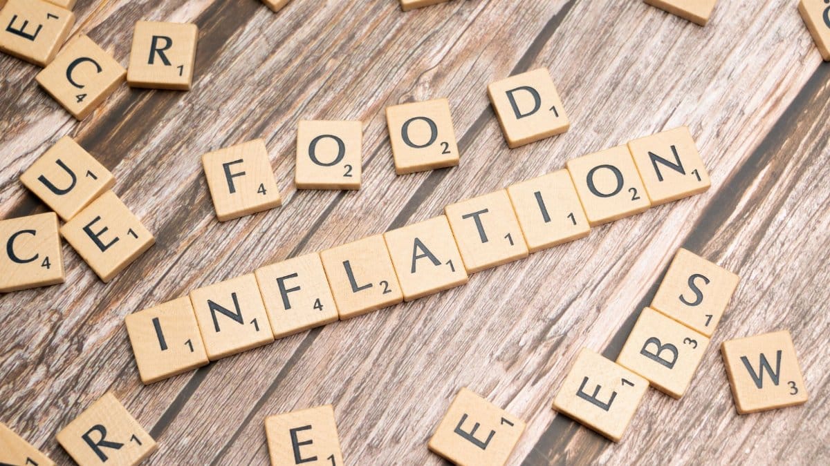 Wooden scrabble tiles arrange to spell 'Food Inflation' on a rustic wooden surface, conceptually depicting rising food prices.