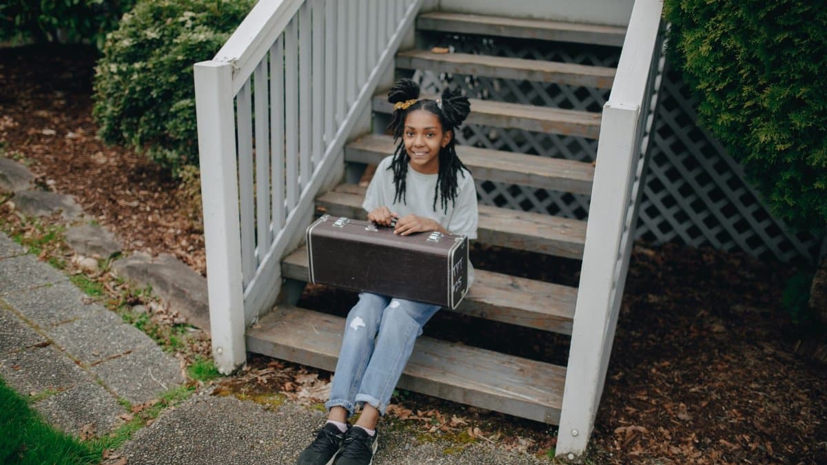 Smiling girl holding trumpet case sitting on outdoor wooden stairs.