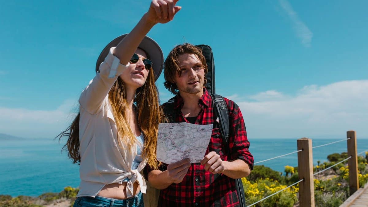 Two young adults exploring a scenic coastal path with a paper map on a sunny day.