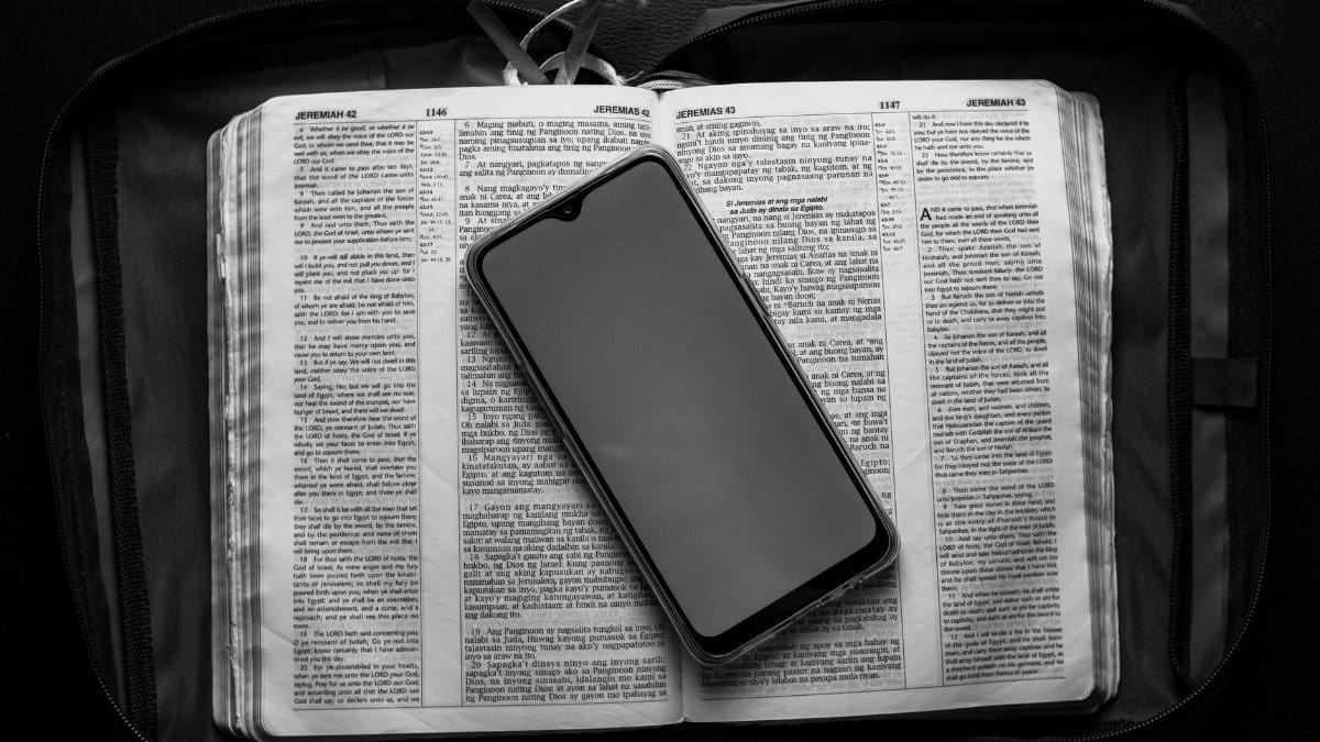 Top view of modern cellphone with empty screen placed on opened textbook in case bag