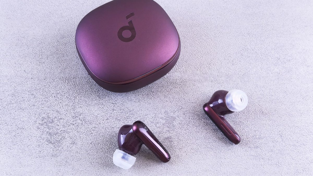 Modern purple wireless earbuds and charging case on a textured concrete surface.