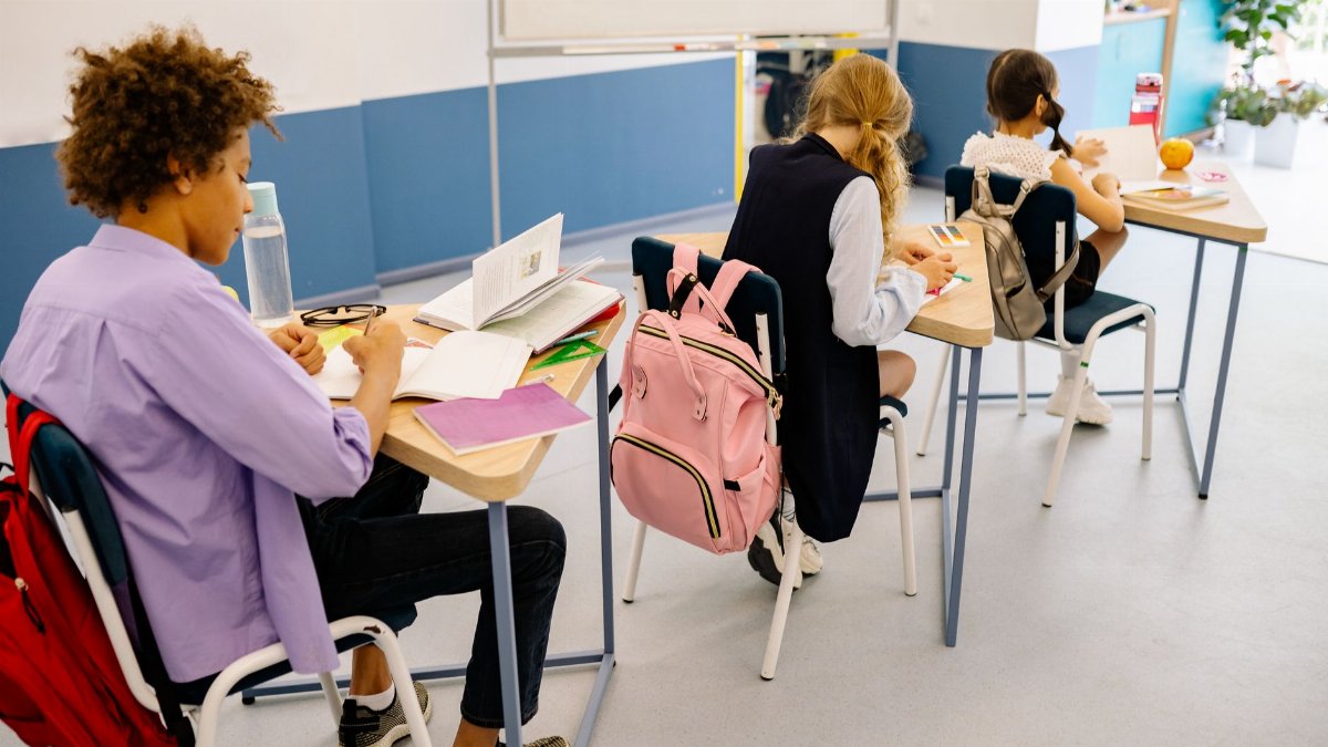 Students attentively studying in a bright classroom with individual desks and backpacks.